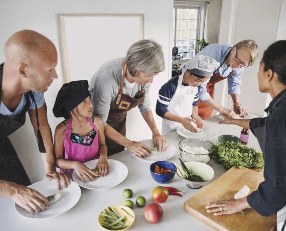 Woman guiding multi-generational family in preparing Asian food at kitchen